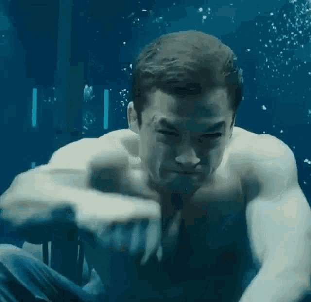 a man without a shirt is swimming underwater while holding something in his hand