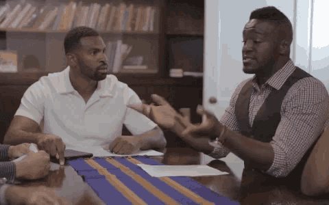 a group of men are sitting around a table and talking