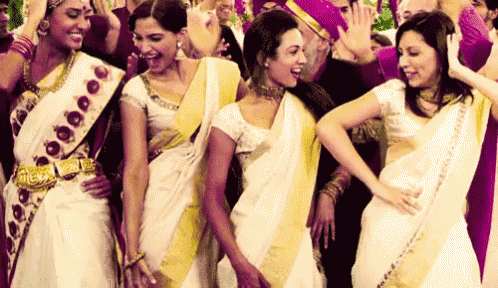 a group of women wearing white and yellow saris are dancing