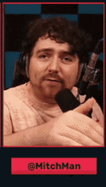 a man with a mustache is holding a microphone and has the name mitchman on the bottom right