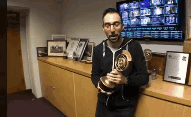 a man in a black sweatshirt holds a trophy in front of a tv screen