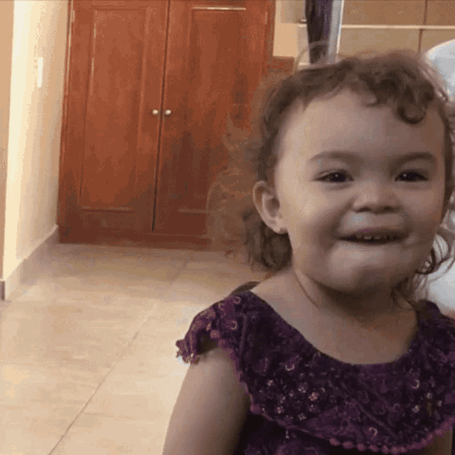 a little girl in a purple dress is smiling and looking at the camera