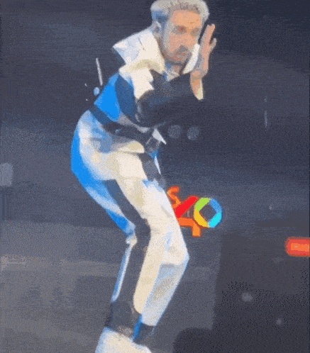 a man in a white suit is holding a microphone and dancing on stage .