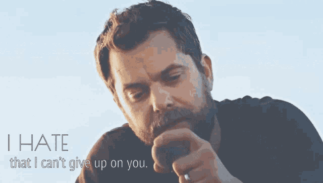 a man with a beard is singing into a microphone with the words i hate that i can 't give up