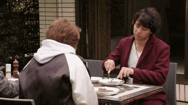 two men sit at a table with plates of food on it