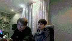 two young men are sitting at a table in front of a computer .