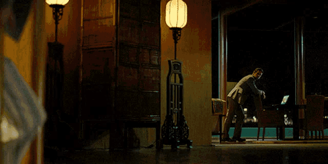 a man in a suit is standing in a dark room with a lamp on the floor