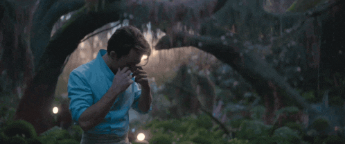 a man in a blue shirt stands in a forest