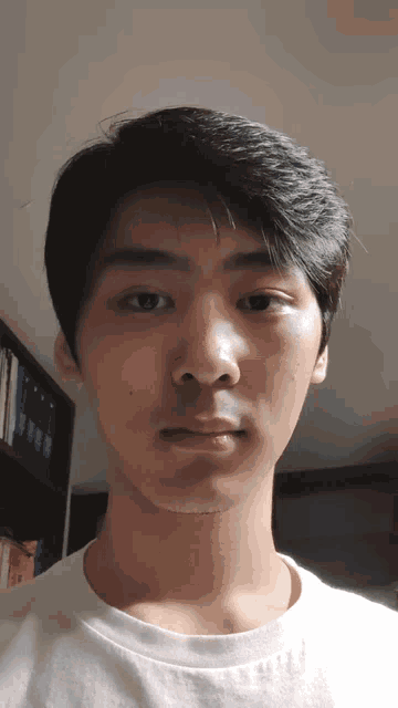 a young man taking a selfie with a bookshelf in the background