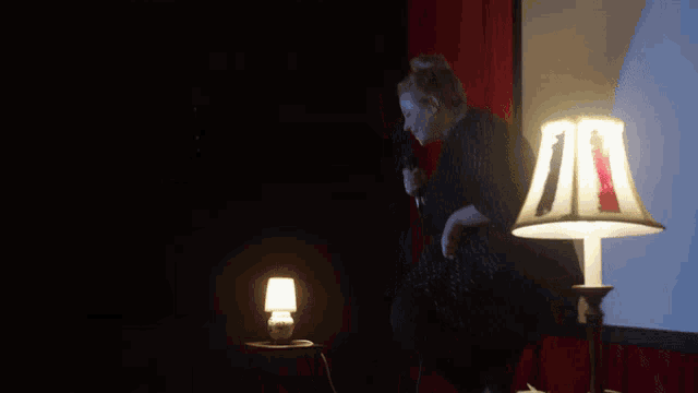 a woman singing into a microphone with a lamp in the background