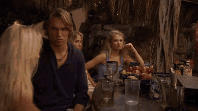 a group of people are sitting at a table with a bowl of fruit in the middle