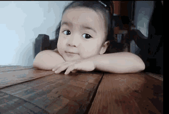 a little girl sitting at a table with her head resting on her hand