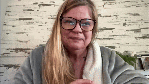 a woman wearing glasses and a robe is sitting in front of a wooden wall