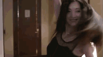 a woman in a black dress is dancing in a room with her hair in the air .