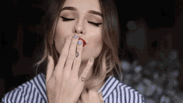 a woman with a tattoo on her finger is blowing a kiss with her hand .