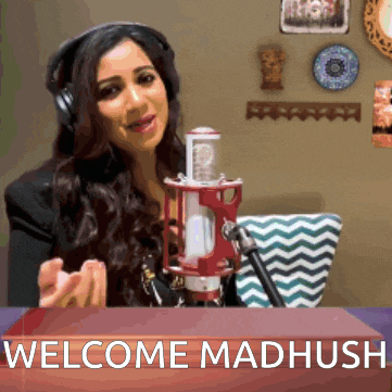 a woman wearing headphones stands in front of a microphone and a sign that says welcome madhush
