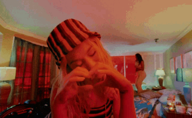 a woman making a heart shape with her hands in a bedroom