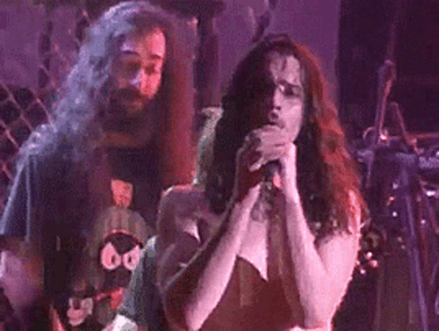 a man with long hair is singing into a microphone on stage
