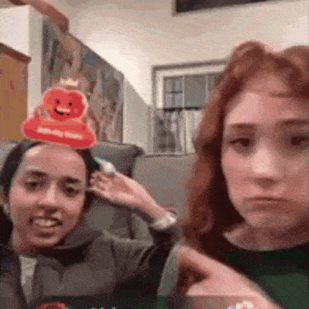 two women are sitting on a couch and one of them has a rubber duck on her head