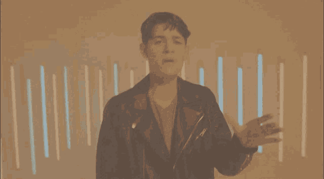 a man in a leather jacket is standing in front of a wall with neon lights
