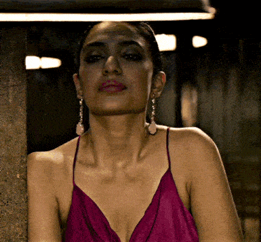 a woman wearing a purple dress and earrings looks at the camera
