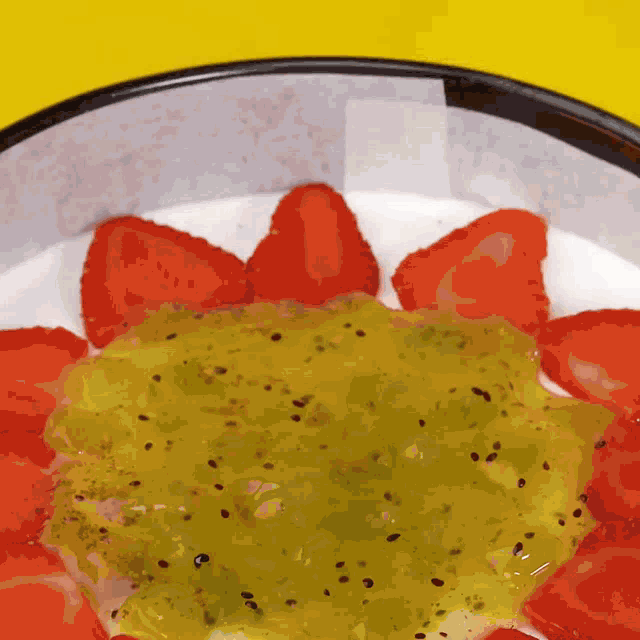 a bowl of strawberries and kiwi sauce on a yellow background