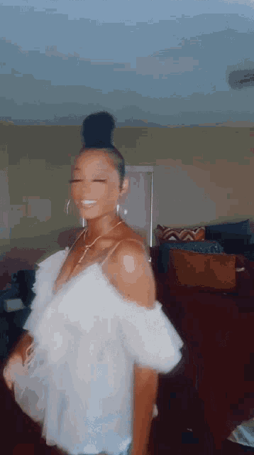 a woman is standing in a living room wearing a white top and earrings .