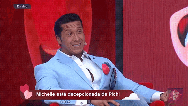 a man in a blue suit is sitting in front of a red screen that says michelle esta decepcionada de pichi