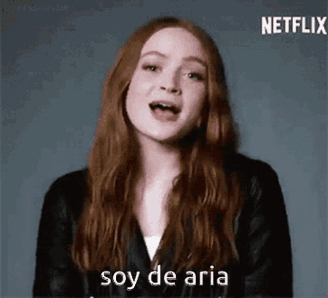 a woman with long red hair is wearing a black leather jacket and says soy de aria .