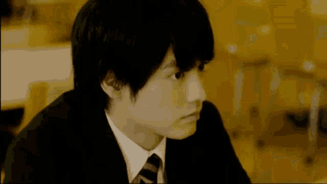 a young man in a suit and tie is sitting in a classroom looking at something .