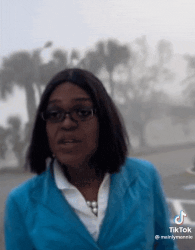 a woman wearing glasses and a blue jacket is standing in front of a foggy background