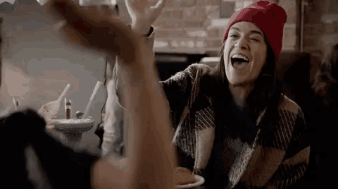 a woman in a red hat is laughing and giving a high five to another woman .