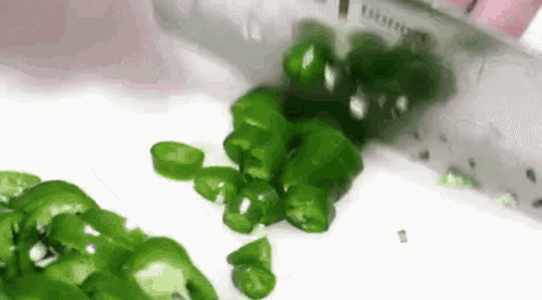 a knife is cutting green peppers on a white surface .