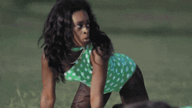 a woman in a green and white polka dot dress is kneeling on the grass .