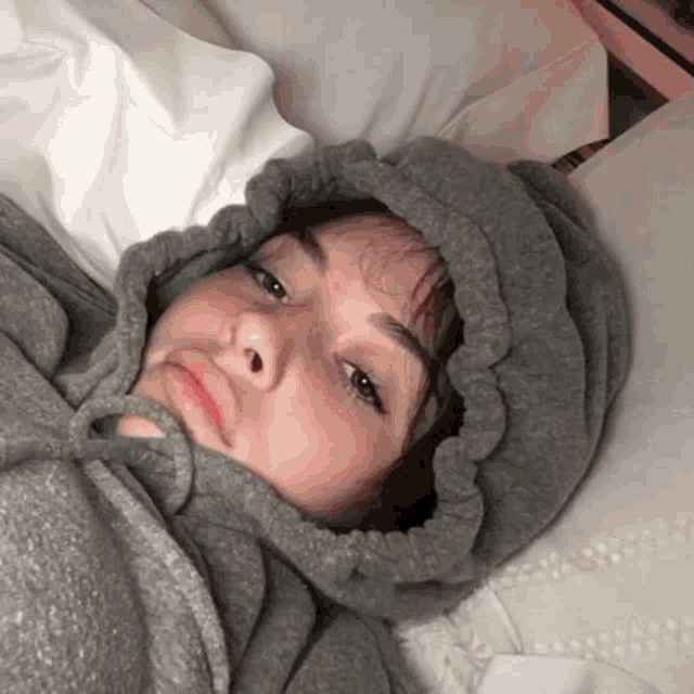 a girl wearing a grey hoodie is laying in bed .