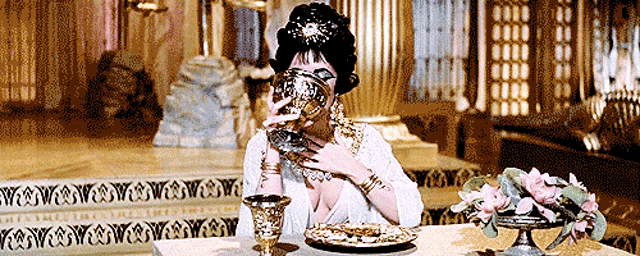 a woman sitting at a table with a plate of food and a cup of wine