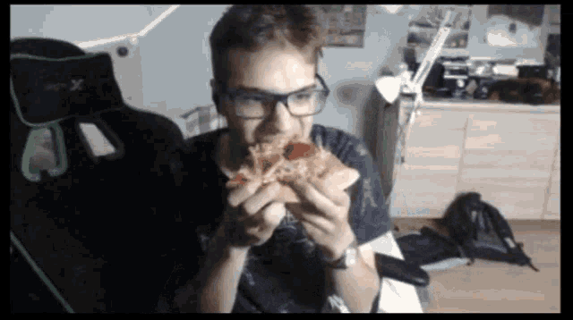 a man wearing glasses is eating a slice of pizza while sitting in a gaming chair