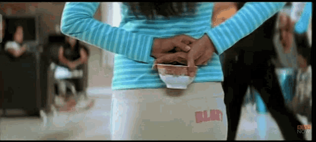 a girl in a blue striped shirt is holding a small bowl on her back