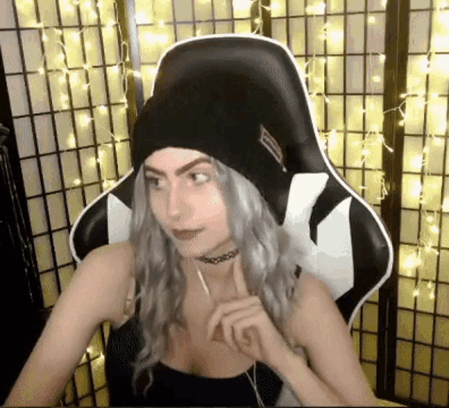 a woman wearing a beanie and choker is sitting in a gaming chair