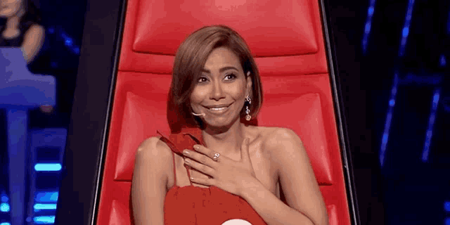 a woman in a red dress is sitting in a red chair and smiling .