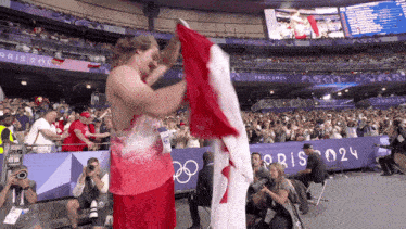a man holds up a canadian flag in front of a crowd at the olympics in paris