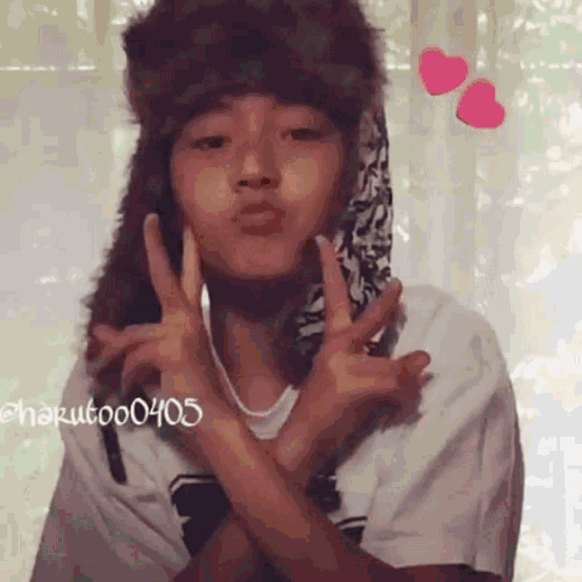 a person wearing a furry hat and a white shirt is making a peace sign with their hands .