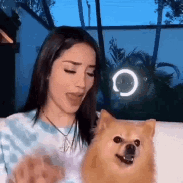 a woman is sitting on a couch holding a small dog and making a funny face .