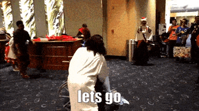 a group of people are gathered in a room with the words let 's go written on the floor