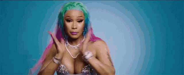 a woman with pink and green hair is standing in front of a blue background and making a funny face .