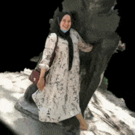 a woman wearing a hijab and a white dress is standing next to a tree .