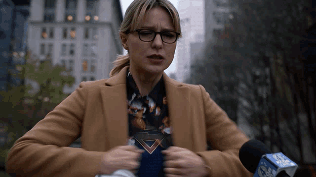 a woman in a tan coat is speaking into a microphone with a cbs logo on it