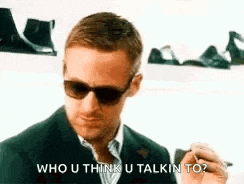 a man in a suit and sunglasses is smoking a cigarette and saying `` who u think u talkin to ? ''