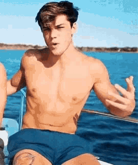 a shirtless man in blue shorts is sitting on a boat .