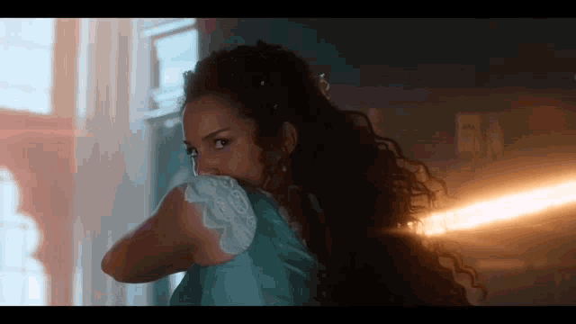 a woman with curly hair is standing in front of a window and covering her mouth with her hand